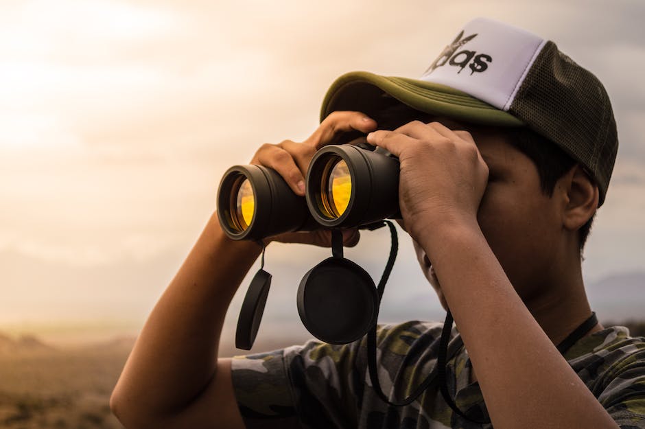 A person looking through binoculars, symbolizing the need for contrarian investors to see beyond what is immediately obvious in the market and find hidden opportunities.