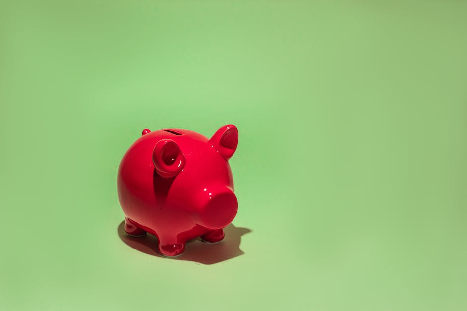 A piggy bank with a broken piece on one side, and a hand coming up from behind it holding cash.