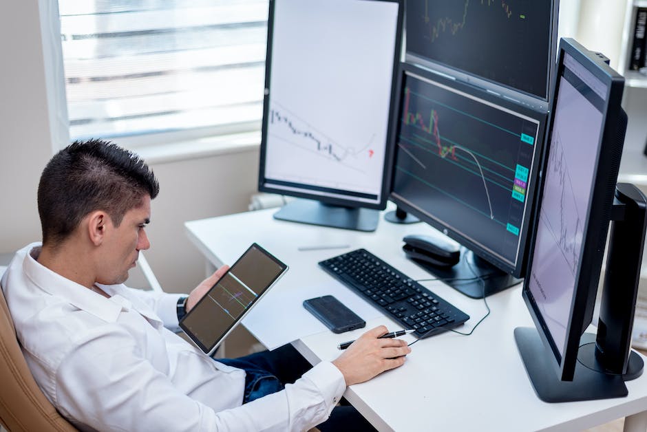 An image of a man sitting at a desk with a computer and financial charts in the background.