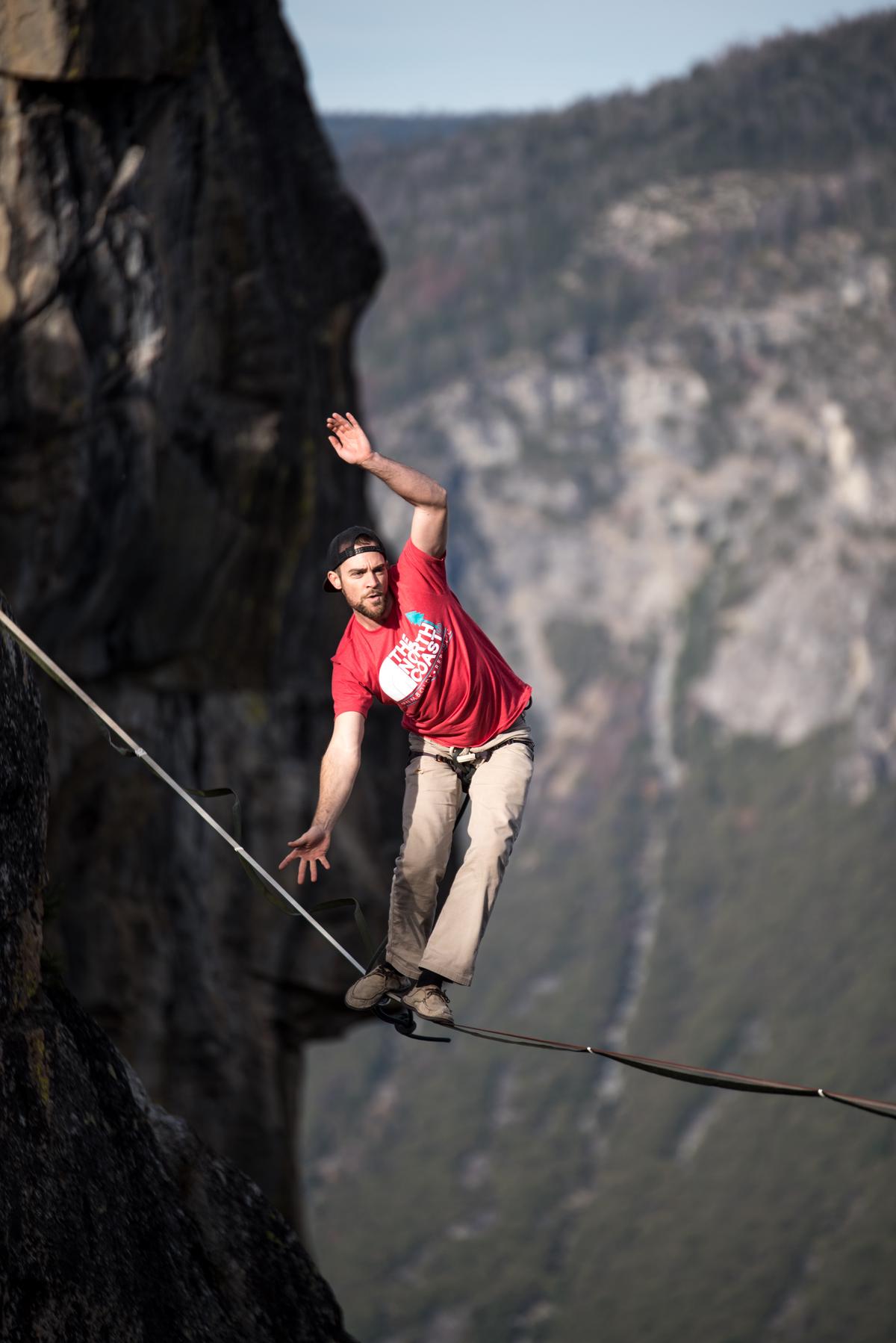 Image depicting a person balancing on a tightrope between two cliffs, representing the risks and challenges of overtrading in trading activities, with dashes instead of spaces
